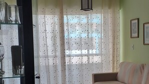 A living room with a sofa, a glass cabinet with items, and a window with curtains. - There's still time to make your reservation for Carnival, excellent apartment, take advantage! (Cabo Frio)