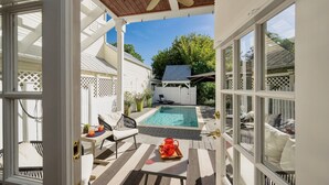 A covered outdoor area with a pool, seating, and a white fence.