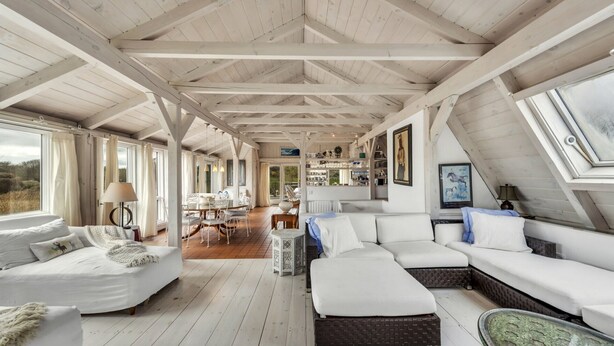 Un loft spacieux avec de hauts plafonds, des poutres apparentes, un coin repas et un espace salon confortable offrant une vue sur l’extérieur.