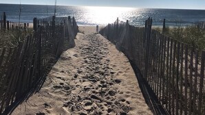 Un sentier de sable bordé de clôtures en bois de part et d’autre, qui mène à l’océan.