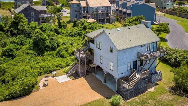 Un quartier résidentiel situé sur la côte, avec une maison remarquable dotée d’un balcon et d’une terrasse, entourée d’une végétation luxuriante et d’autres maisons.