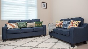 A living room with two blue sofas, a patterned rug, and a window with blinds.