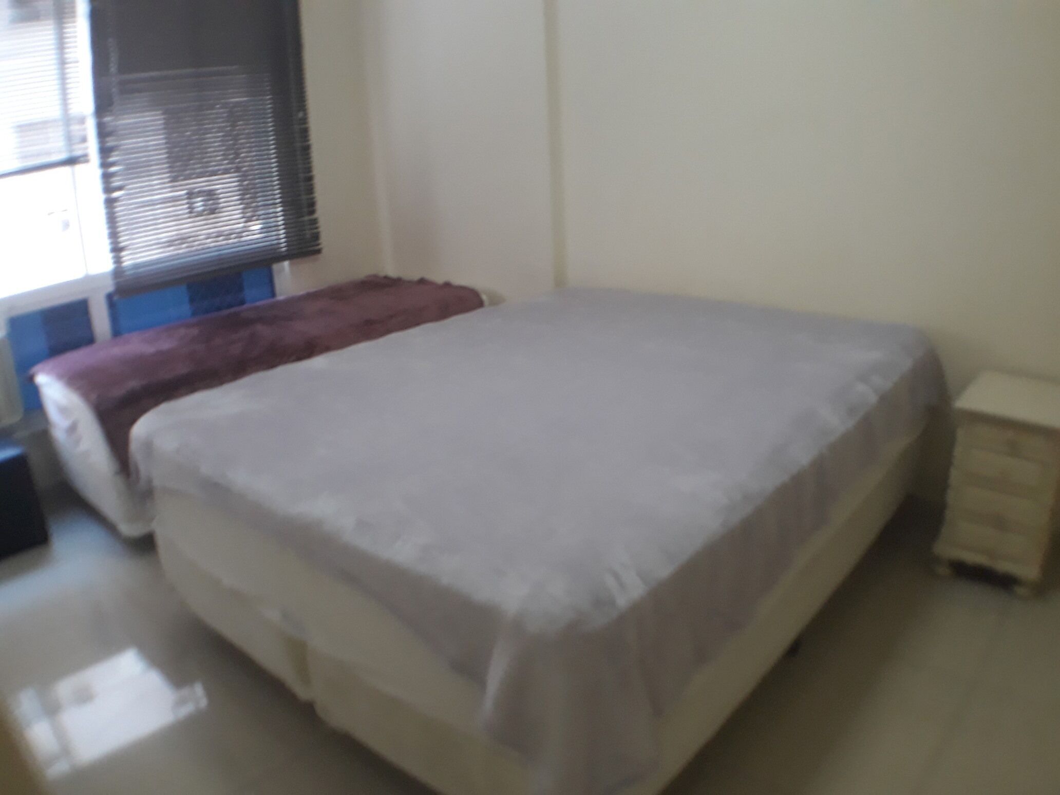 Ein Schlafzimmer mit einem Bett, einem Nachttisch und einem Fenster mit Jalousien.
