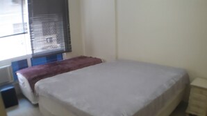 Une chambre à coucher avec un lit, une fenêtre avec des stores et un radiateur.