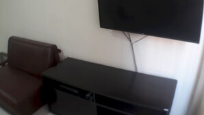 Une pièce dotée d’un téléviseur à écran plat fixé au mur, d’un fauteuil en cuir marron et d’un meuble de rangement noir pour appareils multimédias.