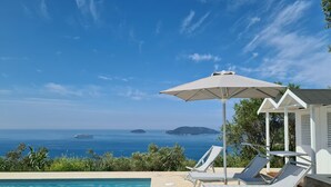 Una piscina con lettini e un ombrellone, con vista su un mare cristallino e isole all'orizzonte.