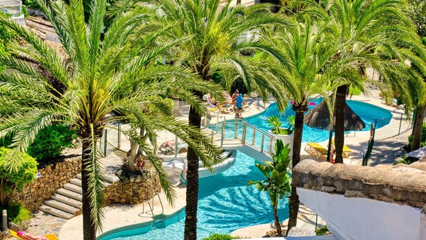 A resort pool area with palm trees, lounge chairs, and a curved pool design. - 1081 Luxurious Beachfront Penthouse with Jacuzzi (Marbella)