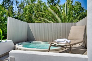 Uma banheira de hidromassagem com uma espreguiçadeira e toalhas, cercada por um muro branco e vegetação.