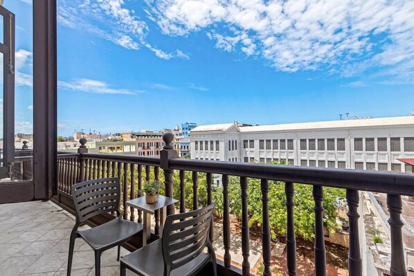A balcony with two chairs and a small table, overlooking a cityscape with buildings and greenery.