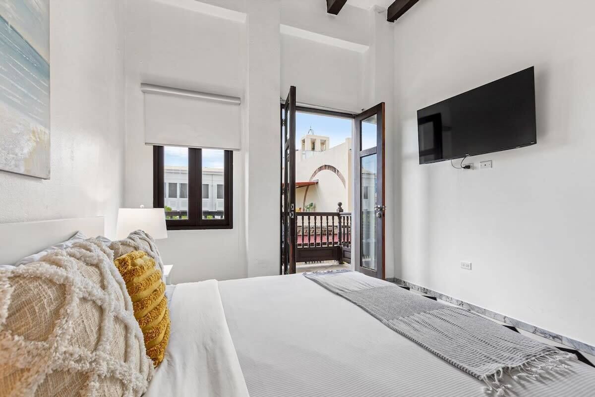Un dormitorio con cama, televisor montado en la pared, ventana y vista a un área exterior.