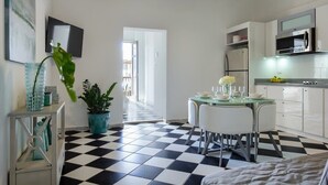 A compact kitchen with a checkered floor, white cabinets, a microwave, and a dining area with a glass table and chairs.