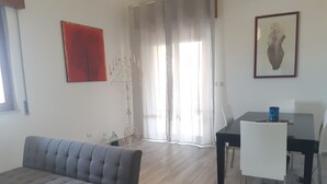 Un salon moderne avec un canapé gris, une table à manger avec des chaises et une grande fenêtre ornée de rideaux légers.