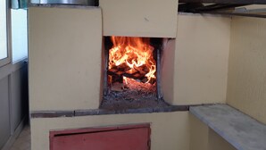 Un poêle à bois dans lequel le feu crépite, une fenêtre avec un rideau et une marmite en métal posée sur le dessus.
