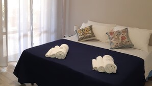 Un lit bien fait, recouvert d’une couvre-lit bleu foncé, avec deux serviettes enroulées et des coussins décoratifs.