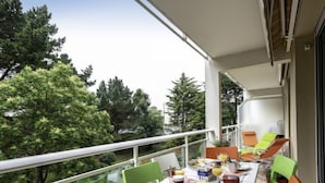 A balcony with a table set for breakfast, surrounded by green chairs, overlooking a forested area. - Port An Dro by Interhome (Carnac)