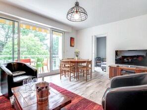 A modern living room with a dining area, a TV, and large windows offering a view of greenery. - Port An Dro by Interhome (Carnac)