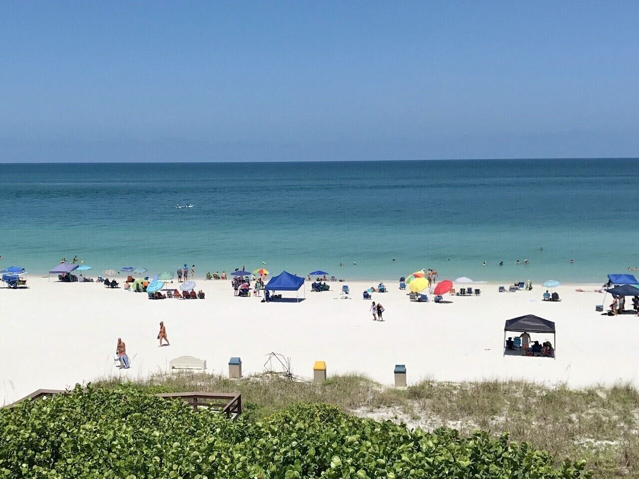 A beach with white sand, clear blue water, and several beach umbrellas.