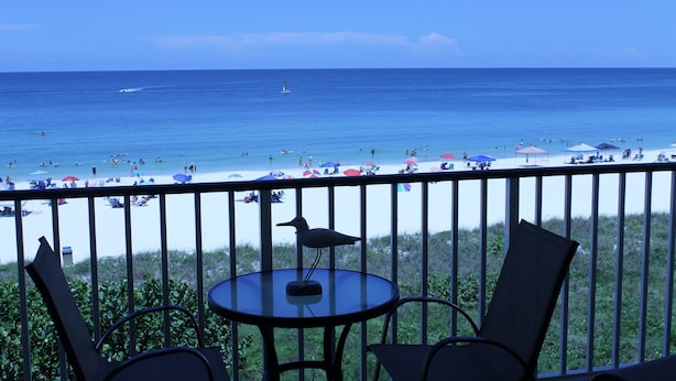 Ein Balkon mit Blick auf einen Strand, einem kleinen Tisch und zwei Stühlen.