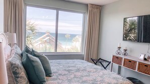 A bedroom with a large bed, a TV mounted on the wall, and a view of the beach.