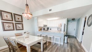 A modern kitchen with white cabinets, a central island, and a dining area with a glass table and wooden chairs.