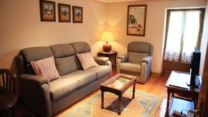 A living room with a sofa, armchair, coffee table, and a lamp. There are framed pictures on the wall and a window with lace curtains. - RURAL HOUSE ARTXEA 2PLTA (Mardea)