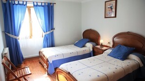 A room with two beds, a wooden chair, a nightstand with a lamp, and a window with blue curtains. - RURAL HOUSE ARTXEA 2PLTA (Mardea)