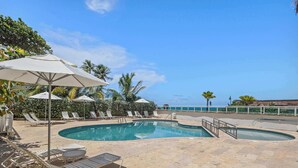 A pool area with lounge chairs and umbrellas, a clear view of the ocean, and a tiled deck. - Oceano Studio  | Oceanfront Studio with Kitchen in Trendy Condado Location (San Juan)