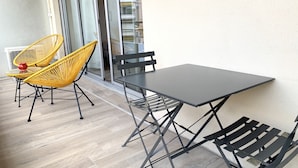 A balcony with a table and two chairs, a sliding glass door, and a view of buildings in the background. - Studio with terrace on the Croisette - Residence du Grand Hotel (Cannes)