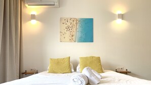 A neatly made bed with white bedding and two yellow pillows, a rolled-up towel, and a wall-mounted air conditioner. - Studio with terrace on the Croisette - Residence du Grand Hotel (Cannes)