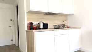 A modern kitchen with white cabinets, a wooden countertop, a coffee maker, a kettle, and a sink. - Studio with terrace on the Croisette - Residence du Grand Hotel (Cannes)