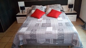 A bed with a quilted blanket, two red pillows, and a headboard with a nightstand on each side. - Close to center, comfort room in air-conditioned villa sauna, billiard, garden (Perpignan)