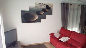 A living room with a red sofa, a flat-screen TV, and a wall-mounted artwork. - Close to center, comfort room in air-conditioned villa sauna, billiard, garden (Perpignan)