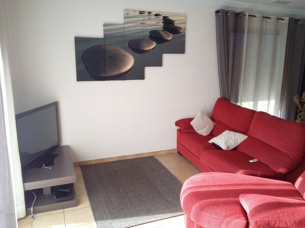 A living room with a red sofa, a flat-screen TV, and a wall-mounted artwork.