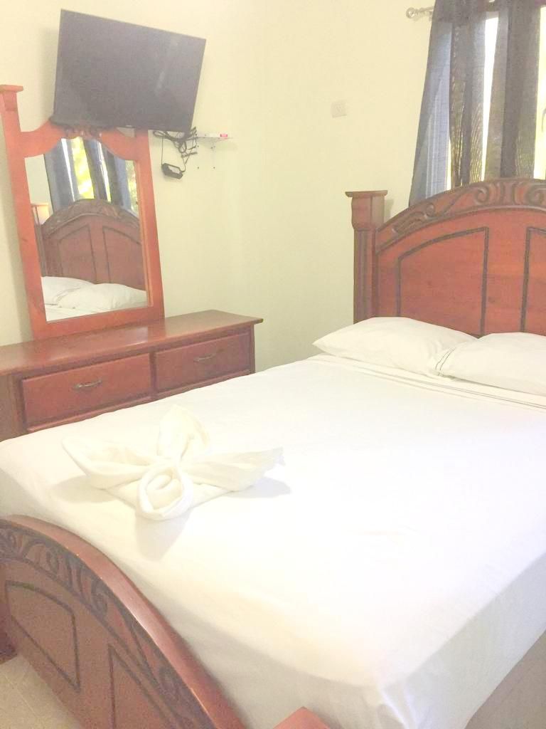 A hotel room with a bed, a wooden headboard, a television mounted on the wall, and a mirror above the dresser.