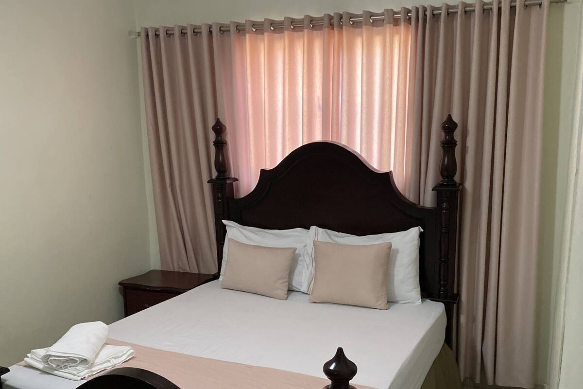 Una cama bien hecha con cabecera de madera, una mesita de noche y un ventilador de techo.