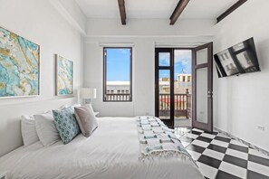 A bedroom with a bed, a TV, and a balcony with a view of buildings.