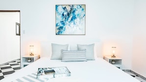 Un dormitorio moderno con una cama grande, dos mesitas de noche con lámparas, un cuadro abstracto enmarcado y un suelo a cuadros.