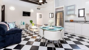 Una cocina moderna con suelo a cuadros blanco y negro, una mesa de comedor con sillas, un ventilador de techo y un televisor montado en la pared.