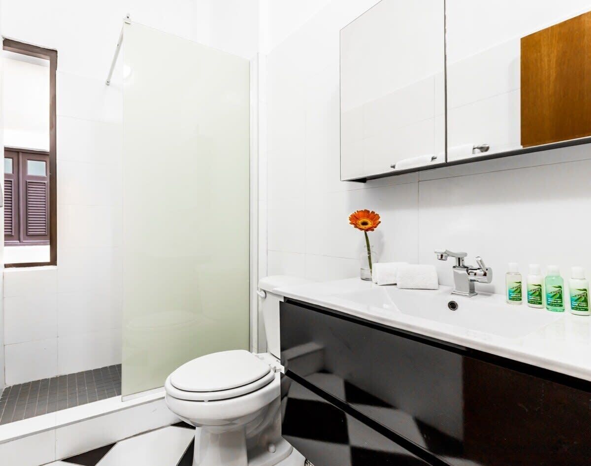 A bathroom with a toilet, sink, and shower. There is a flower on the sink and toiletries on the counter.