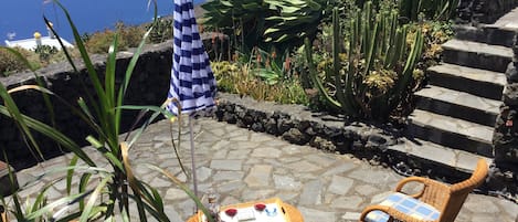 A patio with wicker furniture, a checkered umbrella, and a view of the sea.