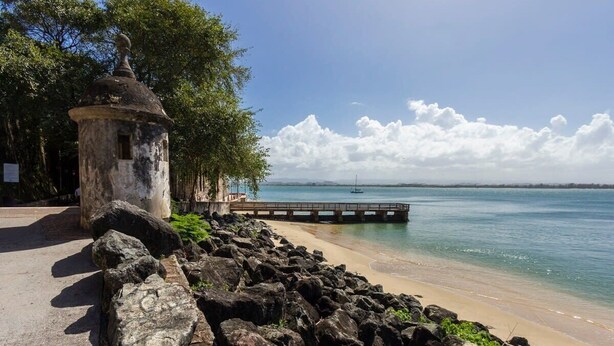 A coastal area with a stone structure, a wooden pier, and a clear view of the sea.