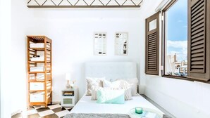 A bedroom with a checkered floor, a bed with white bedding, a wooden shelf unit, and a window with shutters.