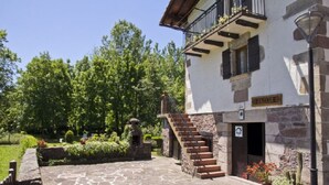A stone building with a staircase leading to a balcony, surrounded by greenery and a cobblestone path. - ARTXEA RURAL HOUSE 1PLTA (Mardea)