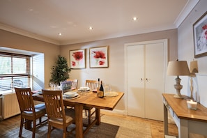 A dining area with a wooden table, chairs, a potted plant, and framed artwork on the wall.