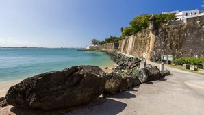 A coastal walkway with a clear view of the sea, a rocky shoreline, and a building with a white facade. - Colonial Suite | 1 BR Apt at Old San Juan (San Juan)