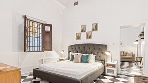 A bedroom with a large bed, a nightstand, a dresser, and a window with blinds. - Colonial Suite | 1 BR Apt at Old San Juan (San Juan)