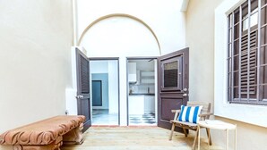 An open doorway leading to a kitchen area with a checkered floor, a bench, and a chair with a striped pillow. - Colonial Suite | 1 BR Apt at Old San Juan (San Juan)