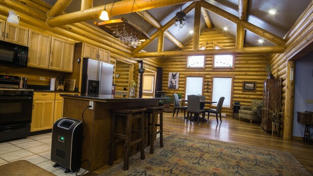A log cabin interior with a kitchen, dining area, and a large window. - Modern log home with a view of the Tetons! (Victor)