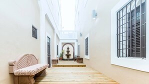 Um corredor estreito com piso de madeira, um banco e uma fonte ao fundo.