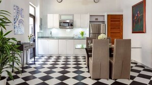 Uma cozinha moderna com armários brancos, eletrodomésticos de aço inoxidável e um chão quadriculado preto e branco.